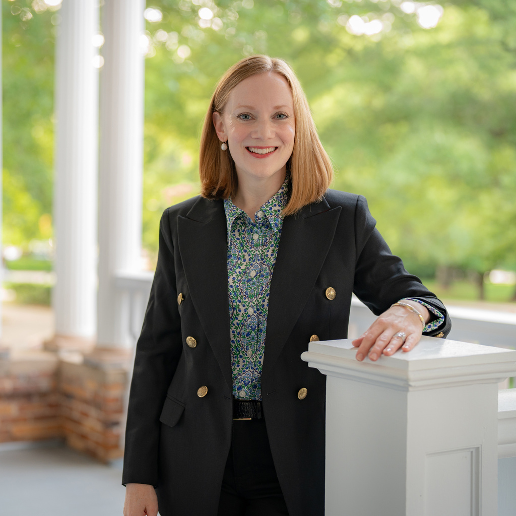 Hopkins wears a suit and stands on a bright university porch