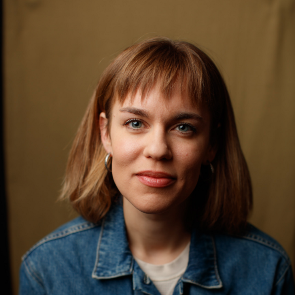 A headshot of a person with bangs, shoulder-length hair wearing a denim shirt.