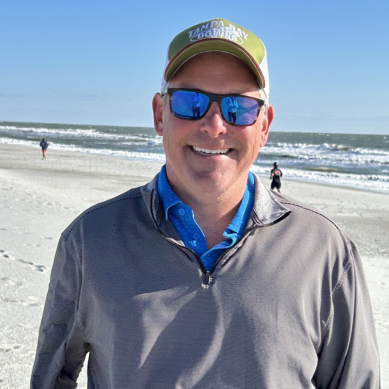 Ted Geltner wears a baseball hat and reflective sunglasses on a beach.