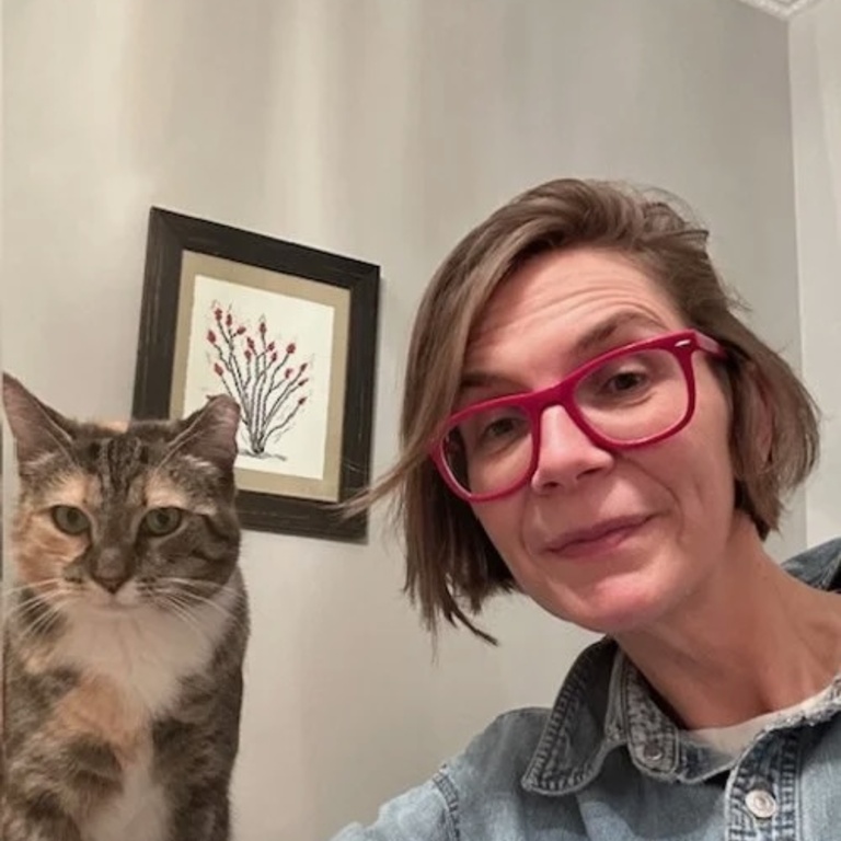 A person wearing red glasses takes a selfie with their tortoise-shell cat